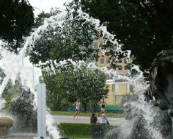 Photo of two runners seen through spray of water fountain.