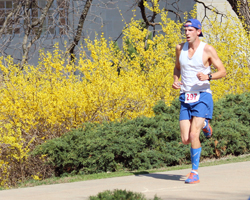 Photo of the lead runner running passed the forsythia in front of Snow Hall.